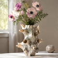 Cream conch-shaped shell vase with projecting forms and pink flowers beside a window