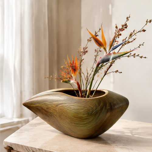 Wide organic wooden vase in golden-brown and olive tones with orange flowers and branches beside a window